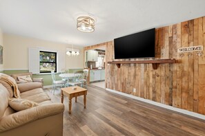 Ein Wohnzimmer mit einer Couch, einem Couchtisch, einem an einer Holzwand montierten Fernseher und einem 'WELCOME'-Schild.