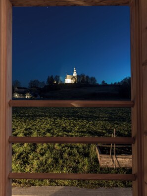 Blick durch ein Fenster auf ein Gebäude, vor ihm ein Feld und im Hintergrund eine Kirche mit Kuppel.