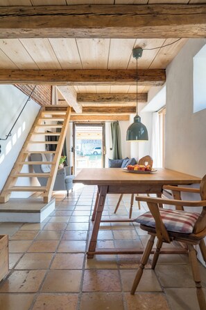 Ein rustikales Interieur mit einer Holztreppe, einem Esstisch mit Stühlen und einer Hängeleuchte.