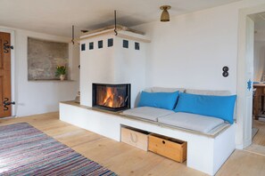 Ein gemütliches Wohnzimmer mit Kamin, einer blauen Kissensofa, Holzboden und einem farbenfrohen Streifen Teppich.