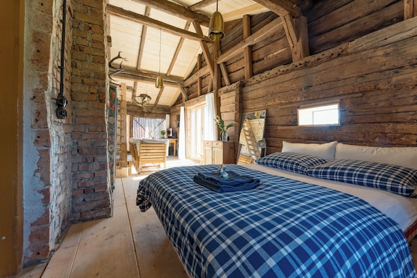 Eine rustikale Holzhütte mit einem großen Bett, einem kleinen Fenster und einer Holzzieldecke.