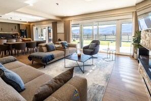 Un vaste espace de vie comprenant un canapé, un fauteuil et une table basse, un coin repas avec des chaises, une cuisine et de grandes portes-fenêtres coulissantes donnant sur un balcon.