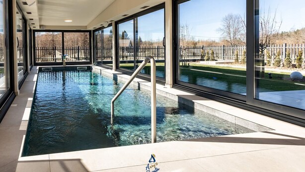 En indendørs swimmingpool med krystalklart udblik, store vinduer og flisegulv.
