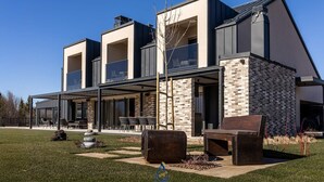 Et moderne hus i to etager med en overdækket terrasse, udendørs møbler og en facade af mursten.