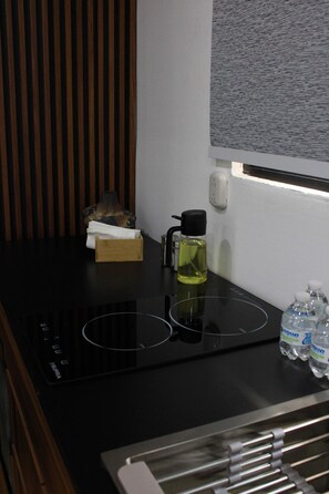 A kitchen area with a black induction cooktop, a wooden box, a bottle of oil, and water bottles on the counter. - Bowra Suite Familiar, Zona Consulado (Zapopan)