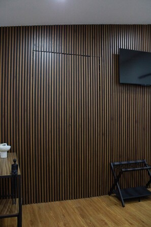 A room with a slatted wooden wall, a flat-screen TV mounted on it, a small table with a cup, and a chair. - Bowra Suite Familiar, Zona Consulado (Zapopan)