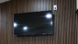 Une pièce dotée d’un téléviseur à écran plat fixé sur un mur composé de lattes de bois, d’un support en métal noir et d’une prise de courant.