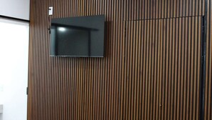 Une pièce dotée d’un téléviseur à écran plat fixé sur un mur en lambris de bois, d’un canapé gris recouvert de tissu et d’un plancher en bois.
