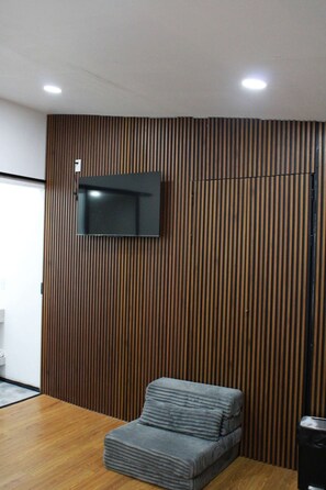 A room with a flat-screen TV mounted on a wooden slat wall, a grey upholstered sofa, and a wooden floor. - Bowra Suite Familiar, Zona Consulado (Zapopan)
