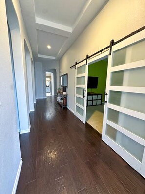 A hallway with wooden flooring, white walls, and a green room door.