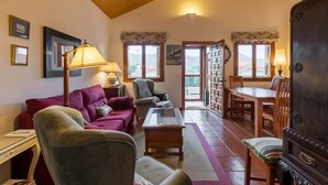 Una sala de estar acogedora con techo de madera, un sofá rojo, un sillón gris, una mesa de centro de madera y un comedor con mesa y sillas.