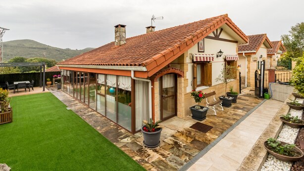 Una casa con techo de tejas, un patio con paredes de vidrio, césped y plantas en macetas.