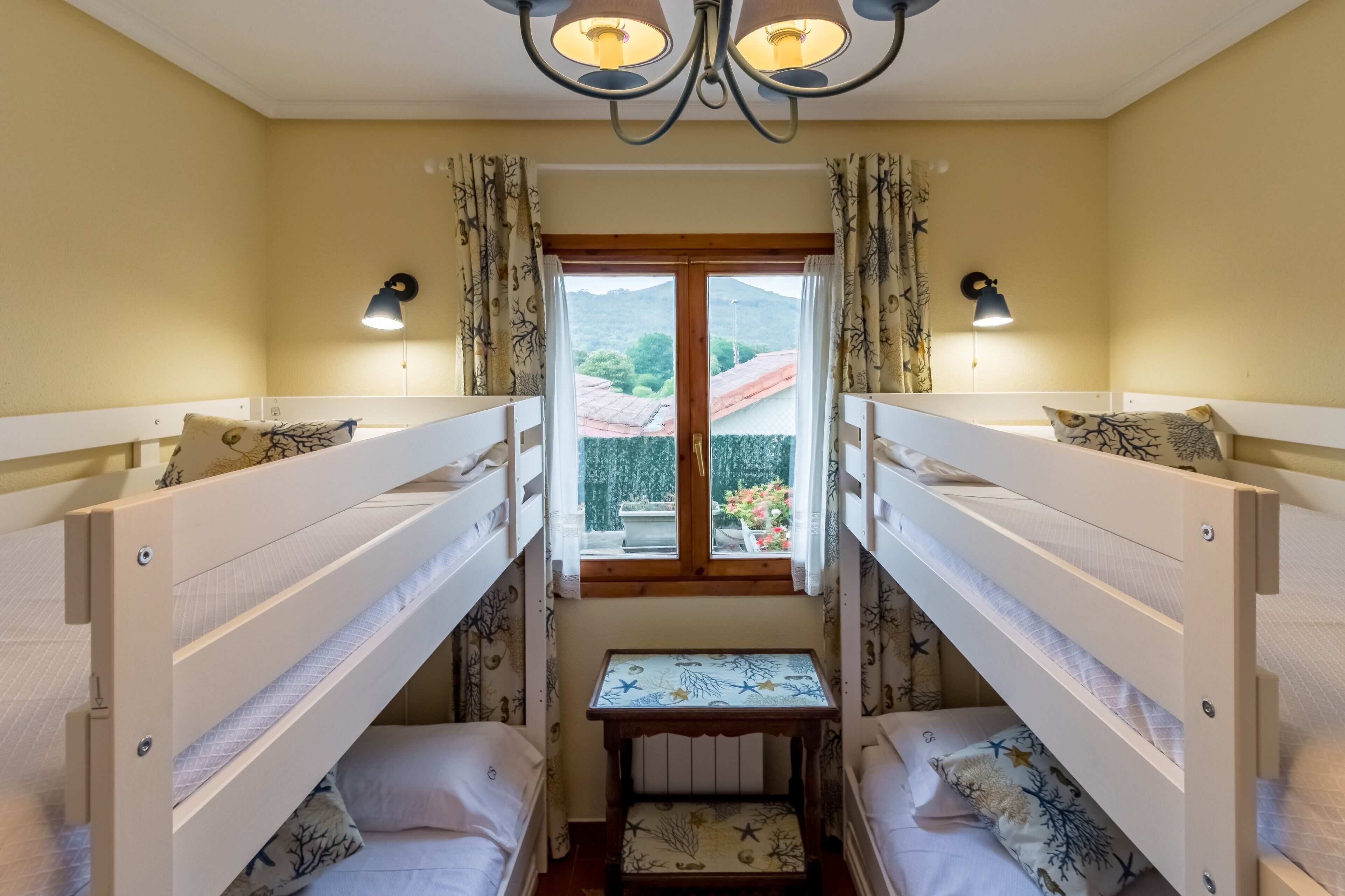 Ein Zimmer mit Etagenbetten, einem kleinen Tisch und einem Fenster mit Vorhängen.