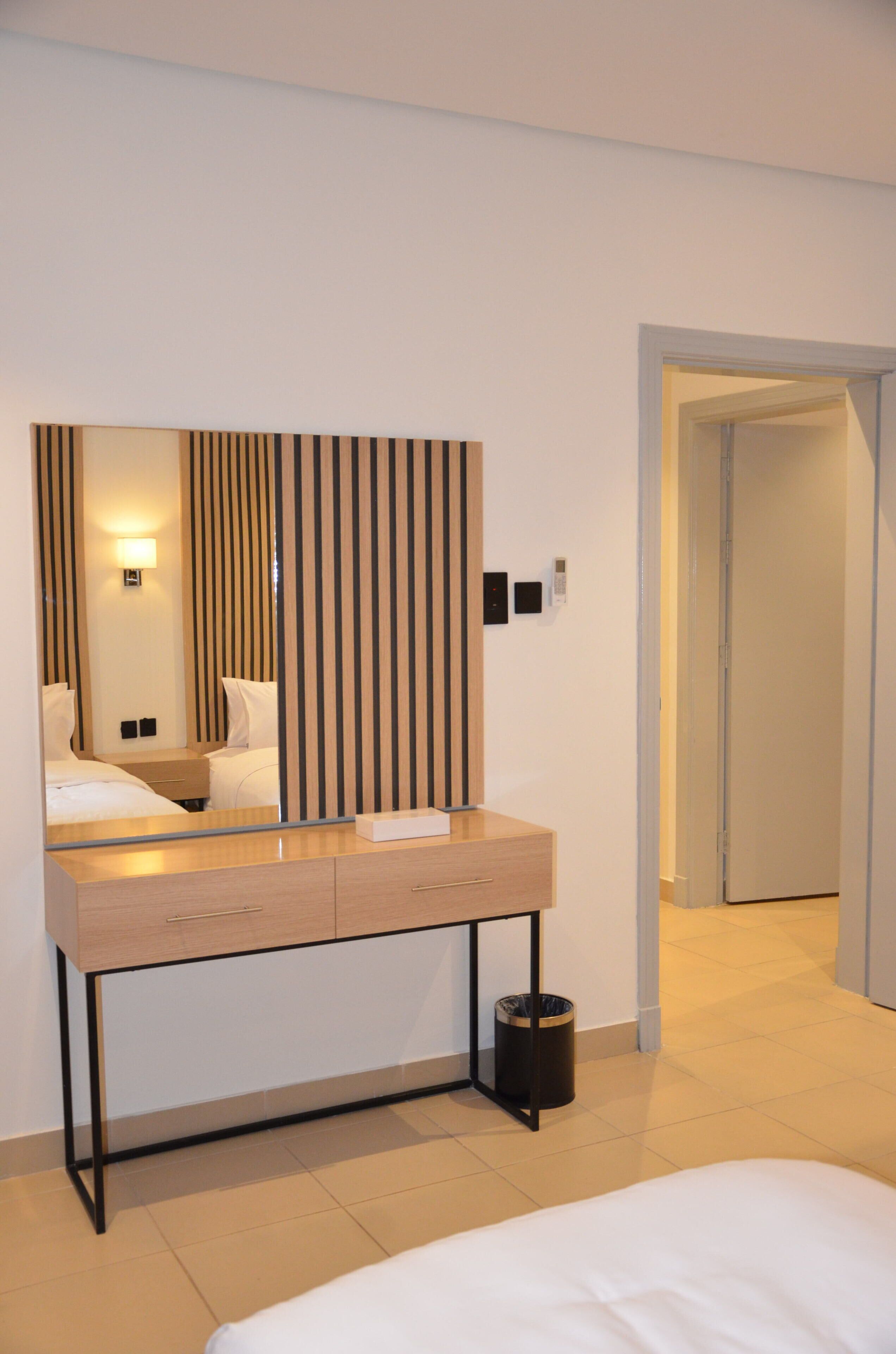 A hotel room with a bed, a bedside table, a mirror, a wall-mounted light, and a door leading to another room.