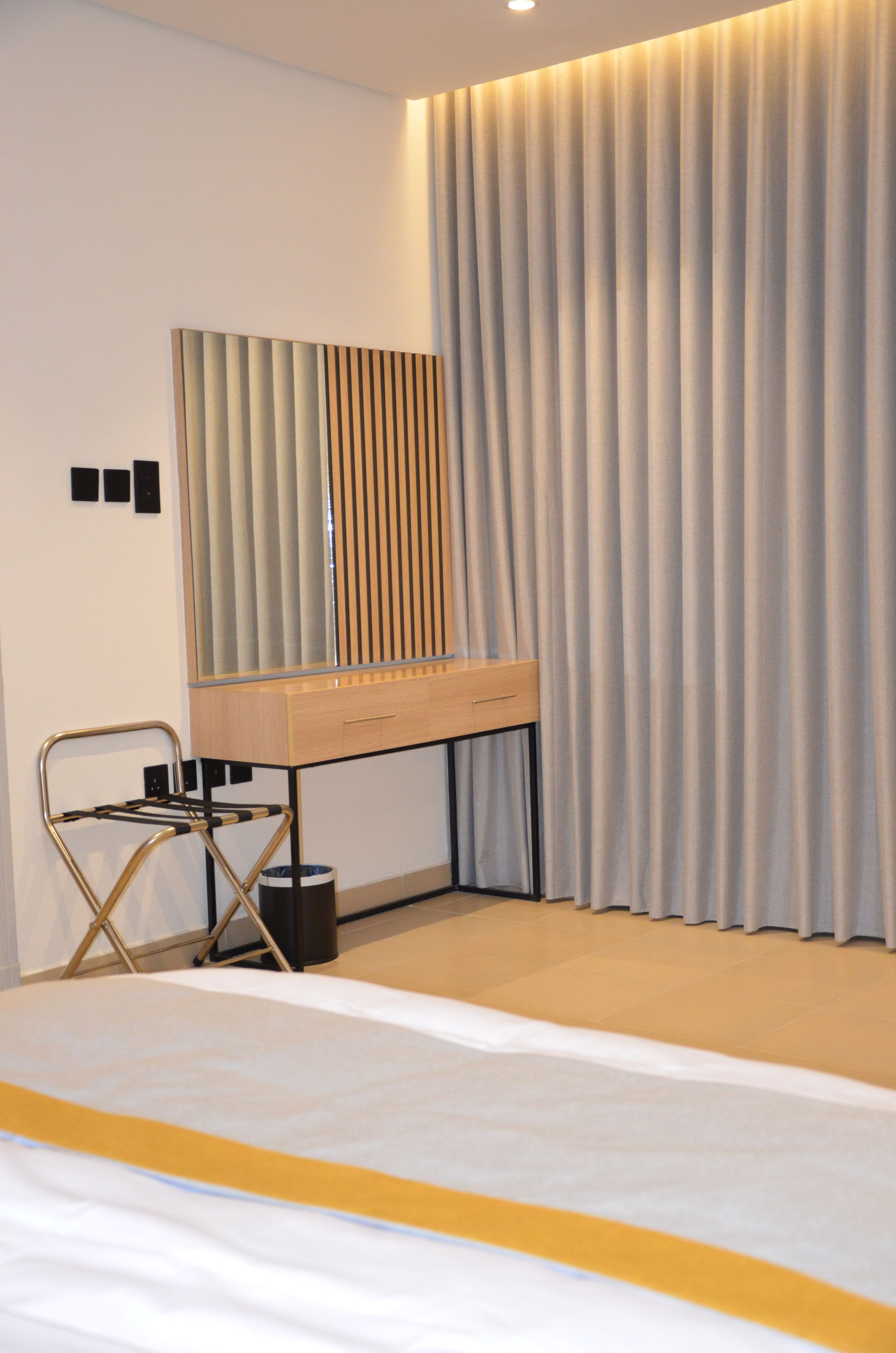 Une chambre moderne avec un lit, un bureau et une chaise, un miroir et une grande fenêtre avec des rideaux.
