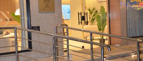A hotel entrance with a metal staircase, a reception desk, and a sign indicating the hotel's name.