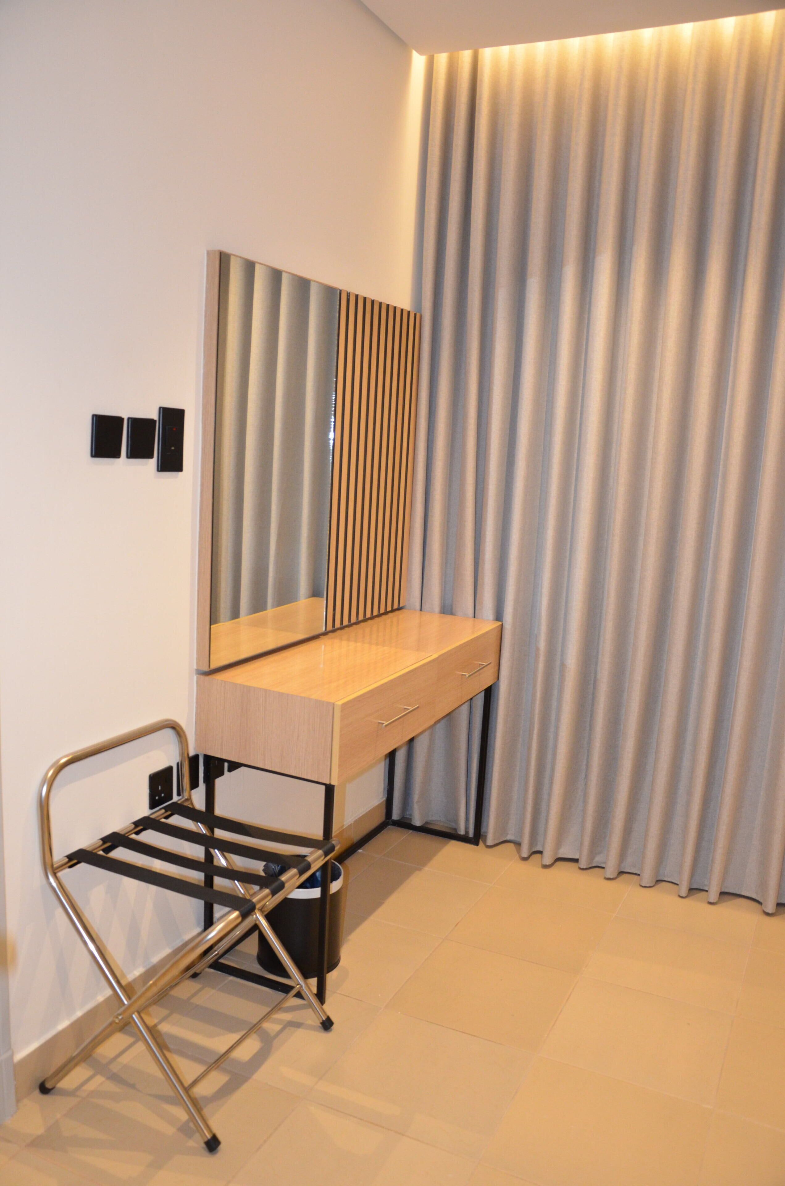 Una habitación compacta con escritorio integrado, una silla, un espejo, un radiador y una cortina.