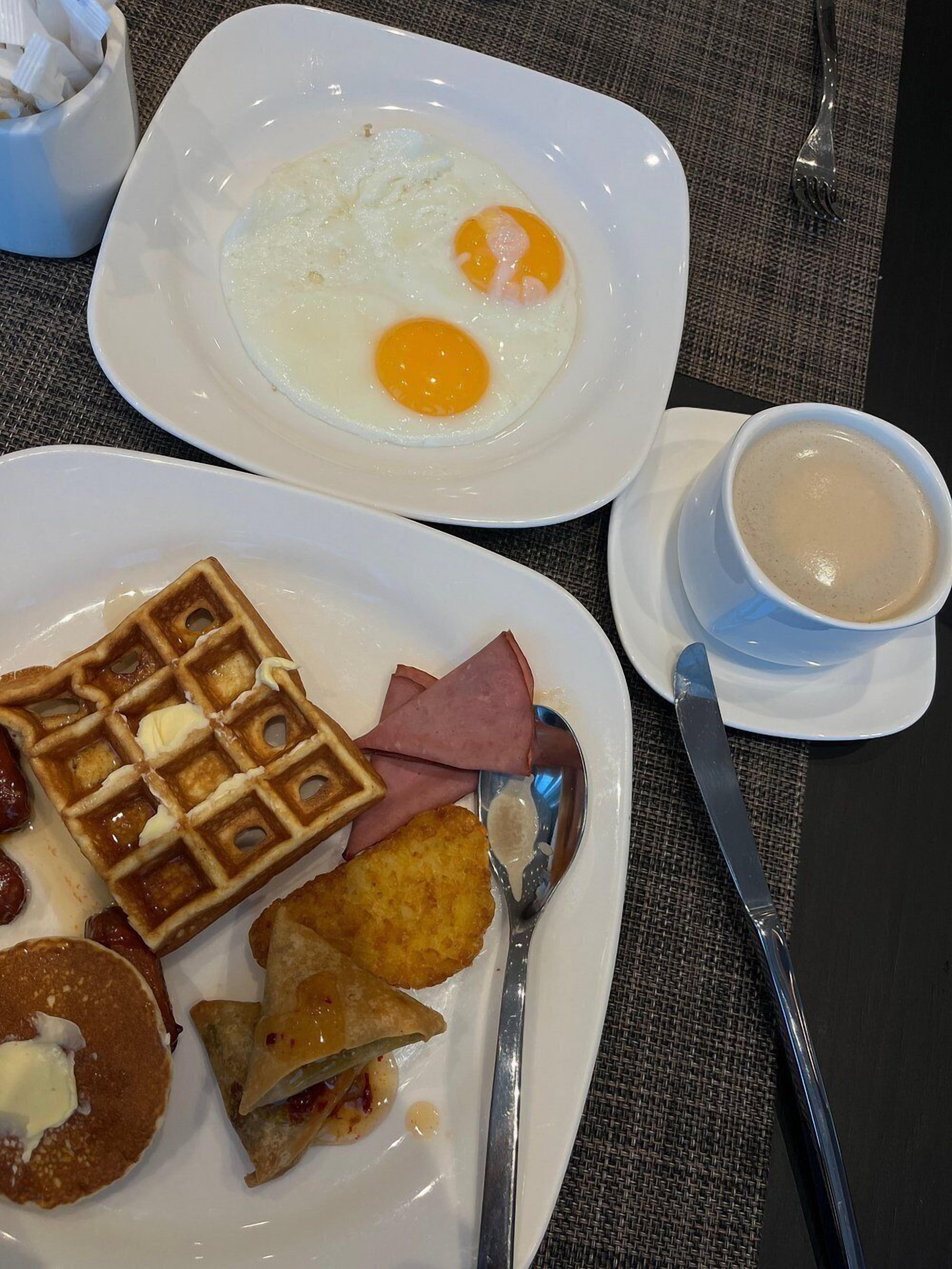 A breakfast plate with eggs, waffles, ham, and pancakes.