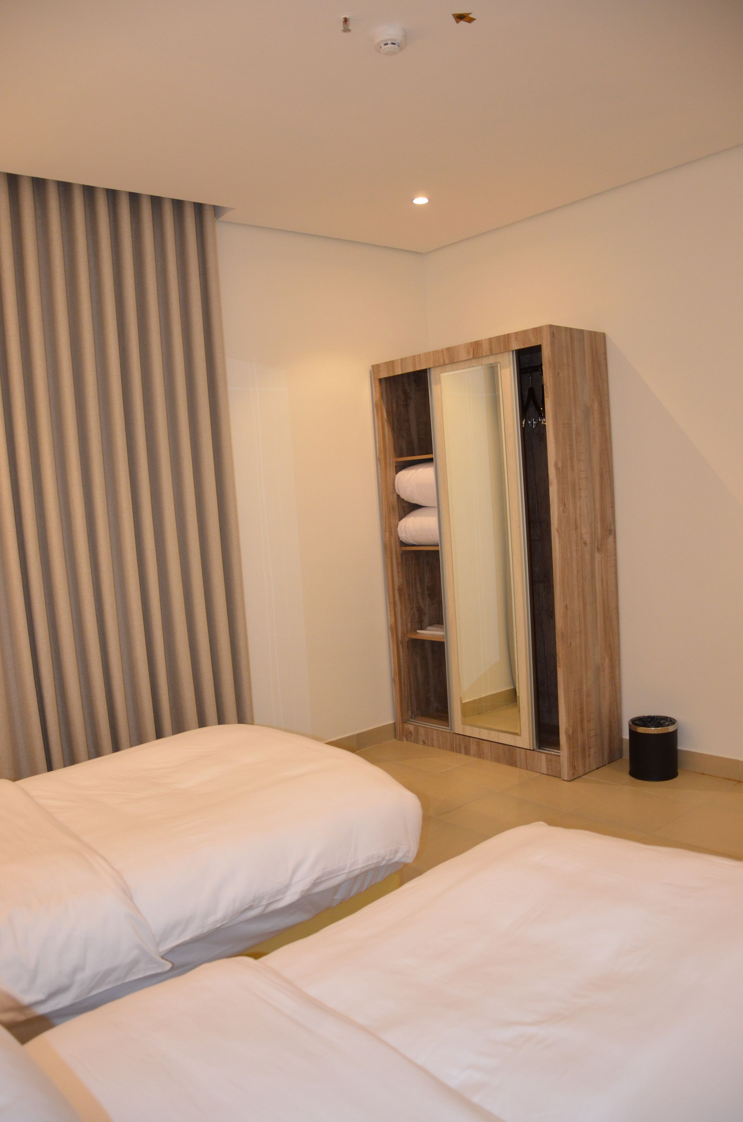 A hotel room with two beds, a wardrobe, a curtain, and a trash bin.