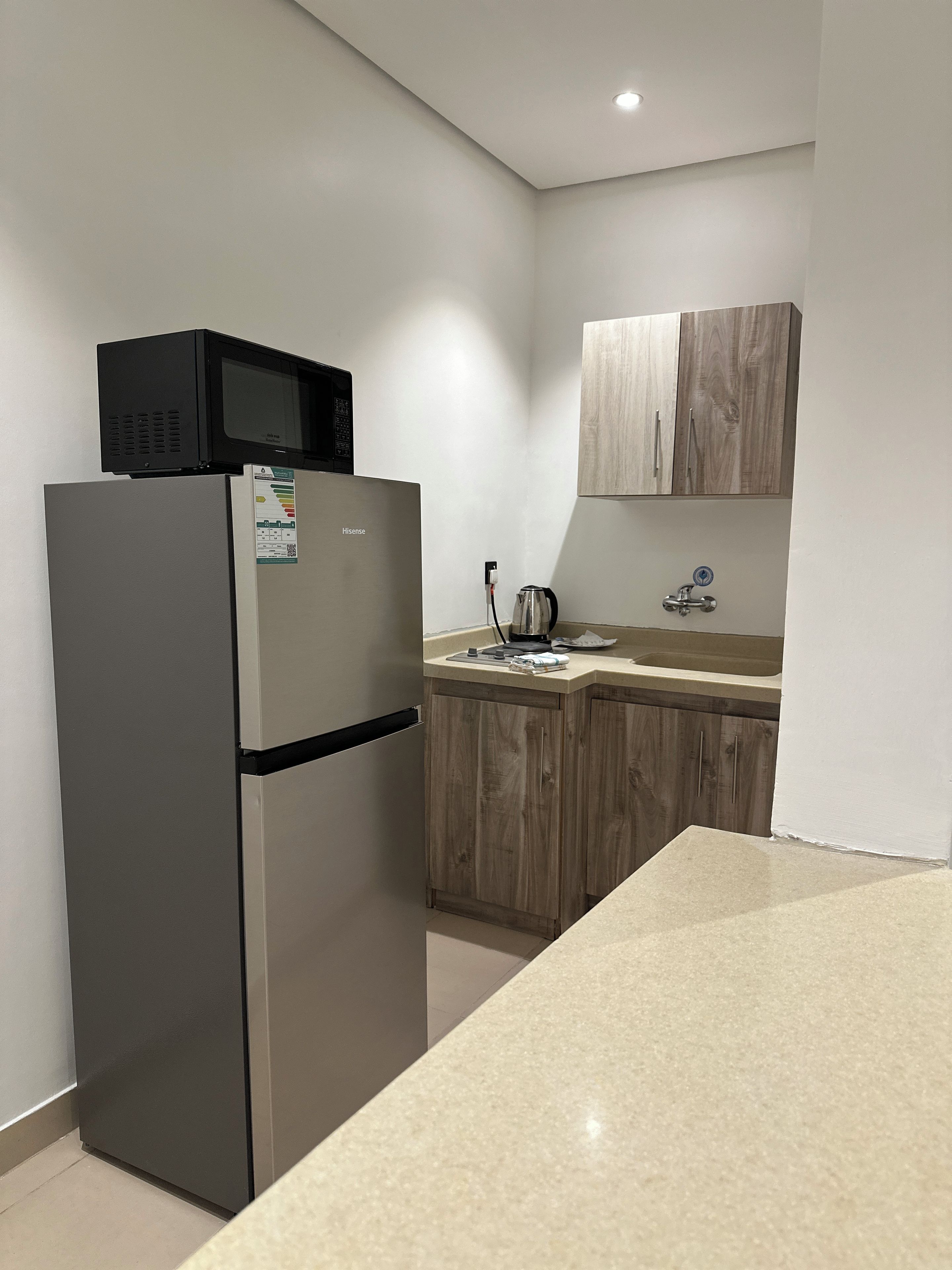 Eine Küche mit einem Edelstahlkühlschrank, einer Mikrowelle, einem Holzschrank und einer Arbeitsplatte.