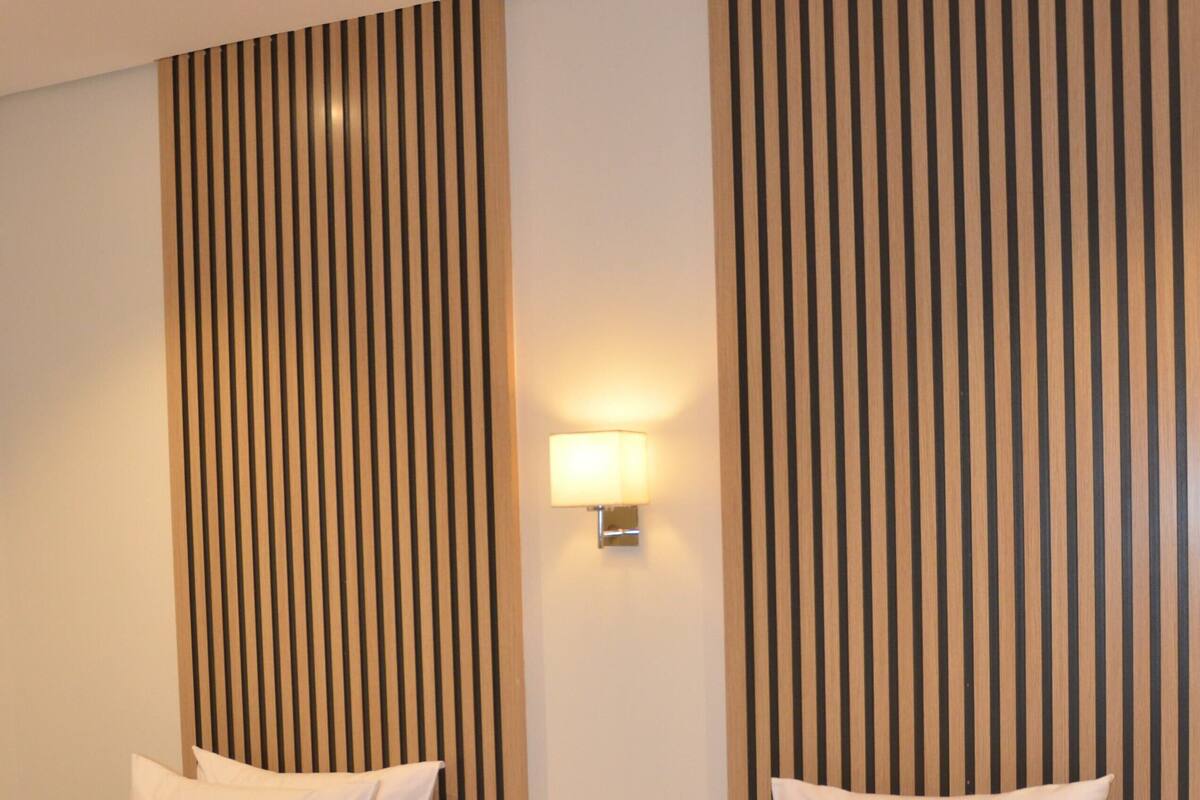 A hotel room with two beds, a nightstand, and a wall-mounted lamp.