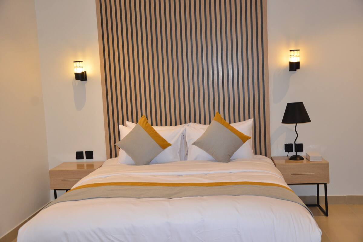 A neatly made bed with a striped headboard, two bedside tables with lamps, and a wall-mounted light fixture.