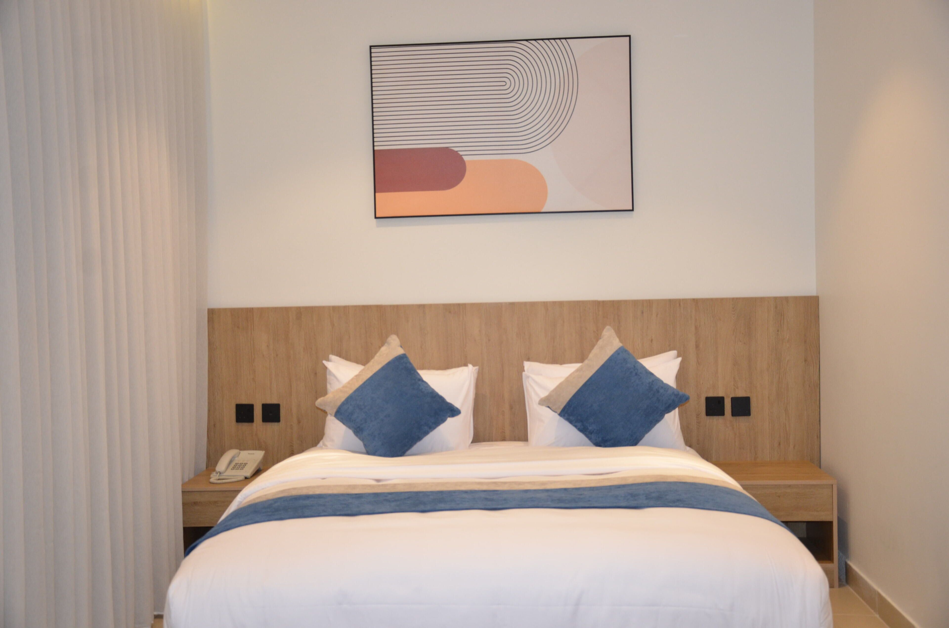 A hotel room with a bed, two bedside tables, a phone, and a wall-mounted abstract artwork.