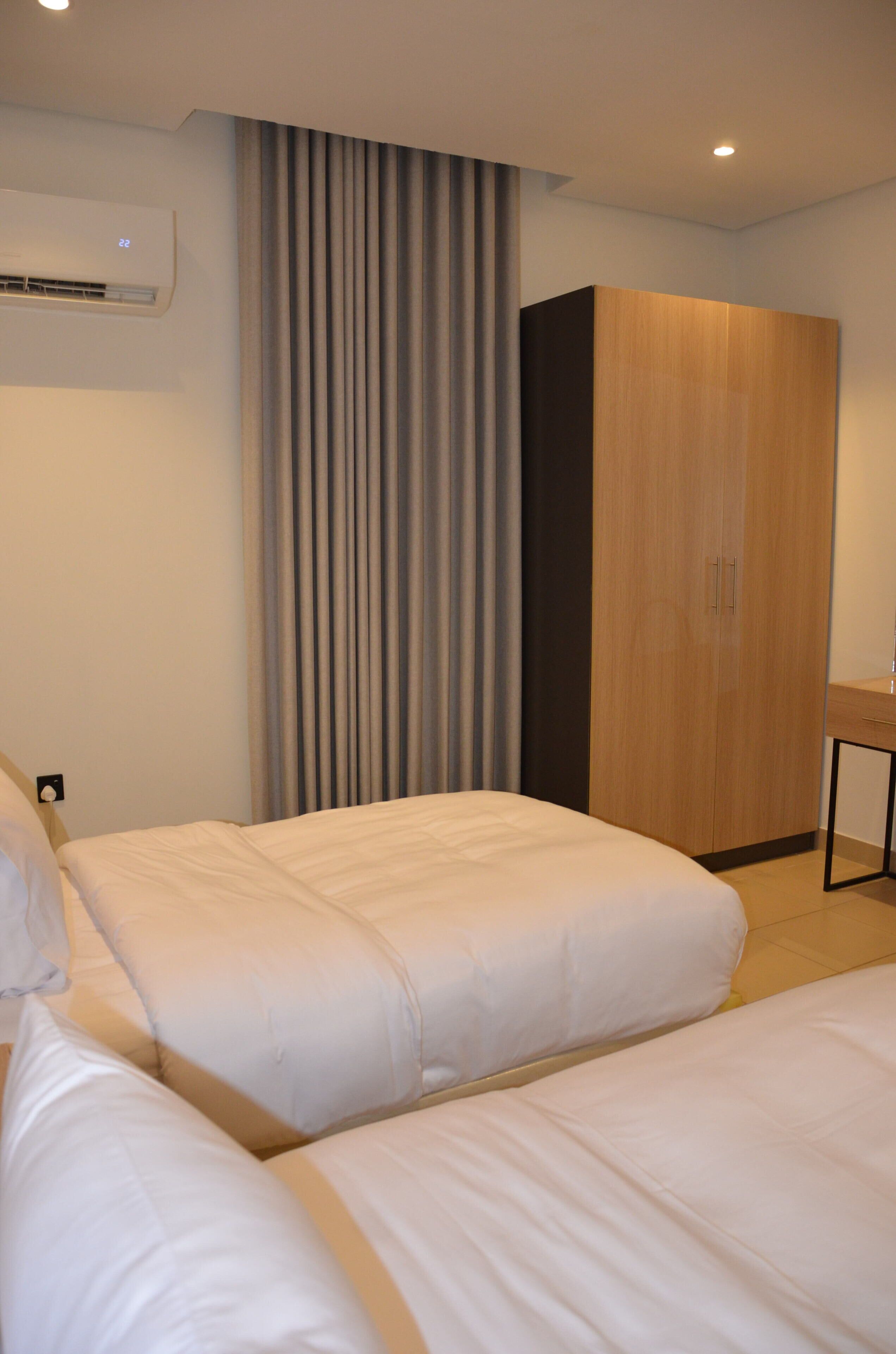 Una habitación de hotel con dos camas, un armario, aire acondicionado y un escritorio.