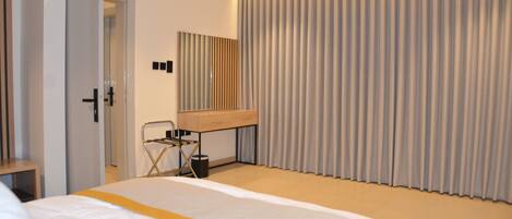 A hotel room with a bed, a desk, a chair, a mirror, and a large window with curtains.