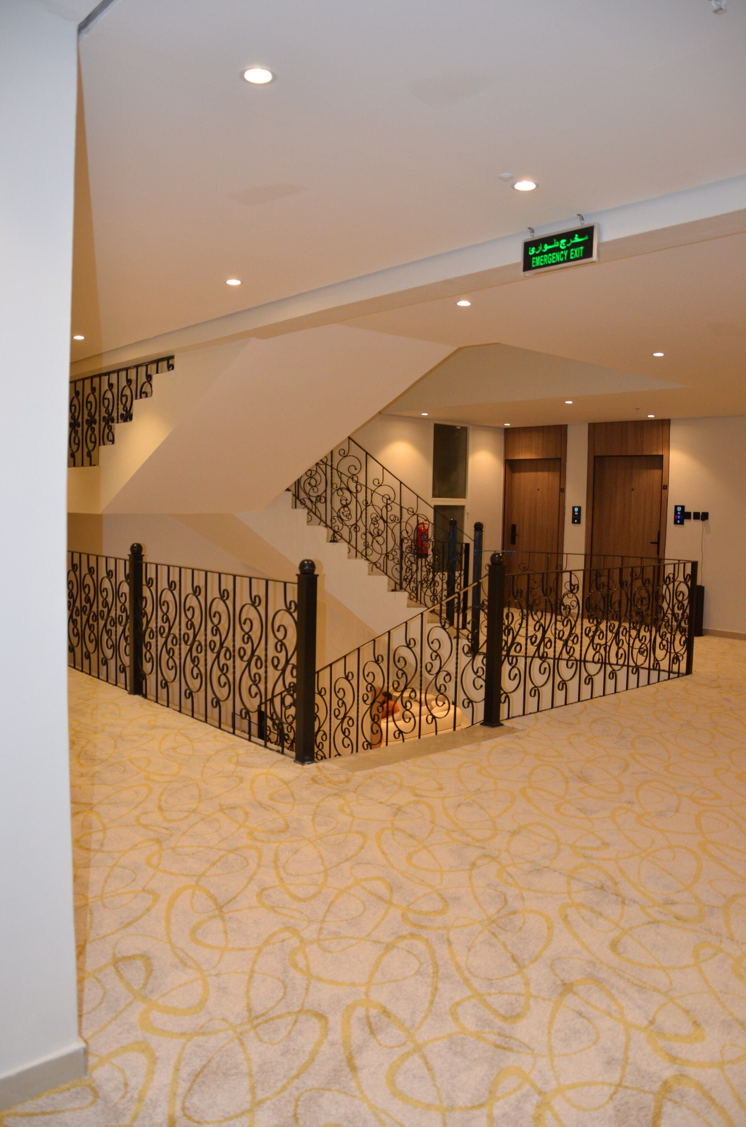 A hotel interior with a staircase, an emergency exit sign, and patterned carpet.