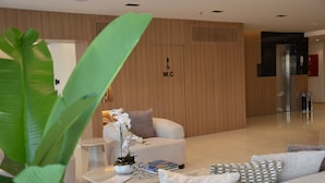 A modern hotel lobby with a reception desk, a seating area with a sofa and armchairs, a coffee table with books and glasses, and a sign indicating a wheelchair-accessible restroom. - Seven Luz Serviced Apartments – Al Masif Branch (Riyadh)
