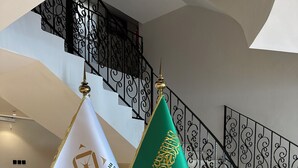A staircase with ornate black railings and two flags on stands.