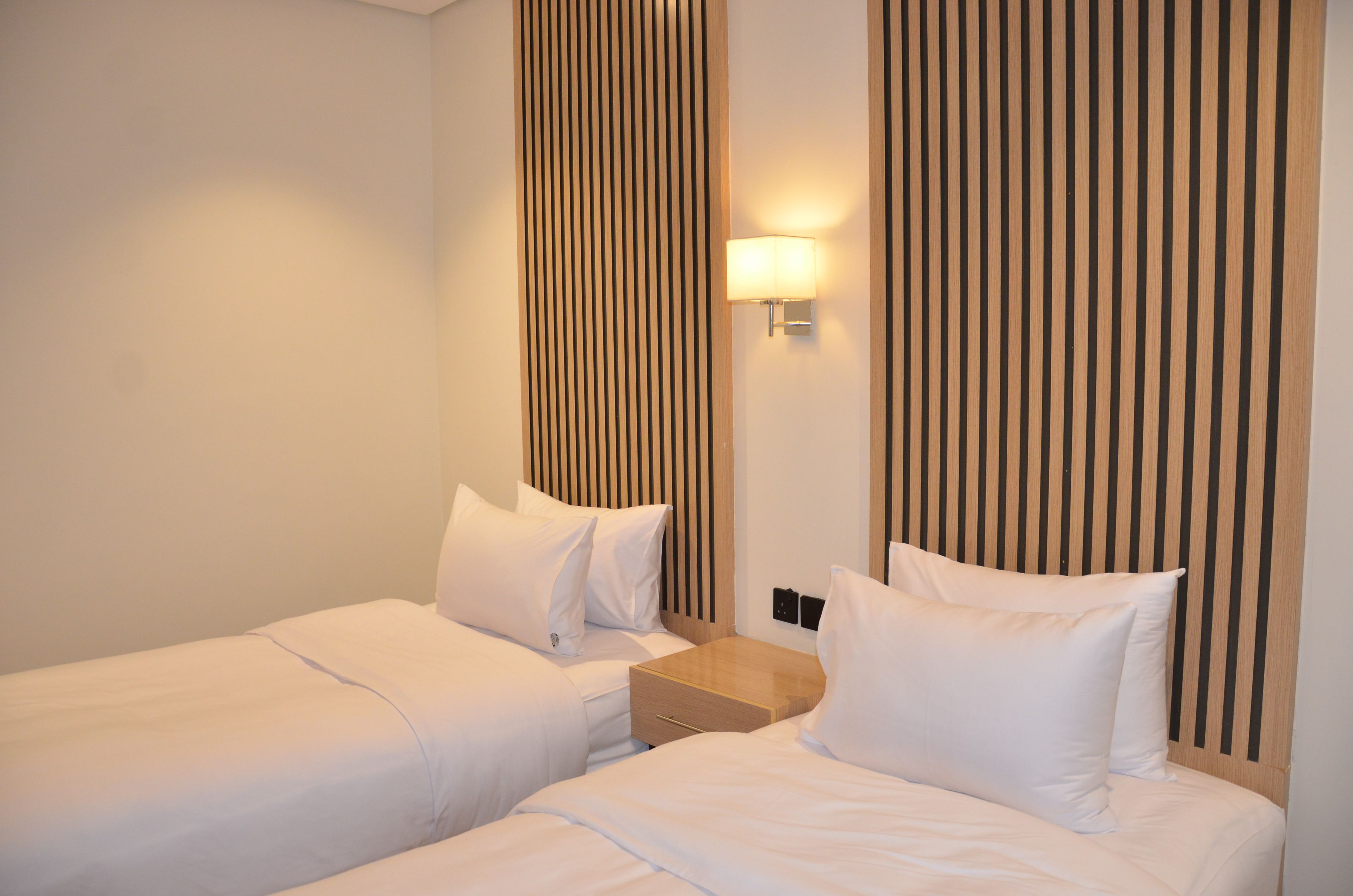 Une chambre d’hôtel avec deux lits, une table de chevet, une lampe fixée au mur et des lambris en bois verticaux.