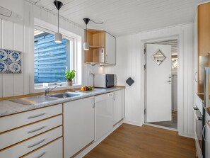 A modern kitchen with white cabinetry, a wooden countertop, a sink, a microwave, and a window with blue shutters. - "Aiden" - 650m from the sea by Interhome (Fanø)