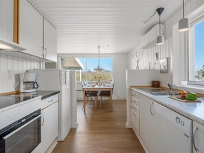 A modern kitchen with white cabinetry, a built-in oven, a coffee maker, and a dining area with a table and chairs. - "Aiden" - 650m from the sea by Interhome (Fanø)