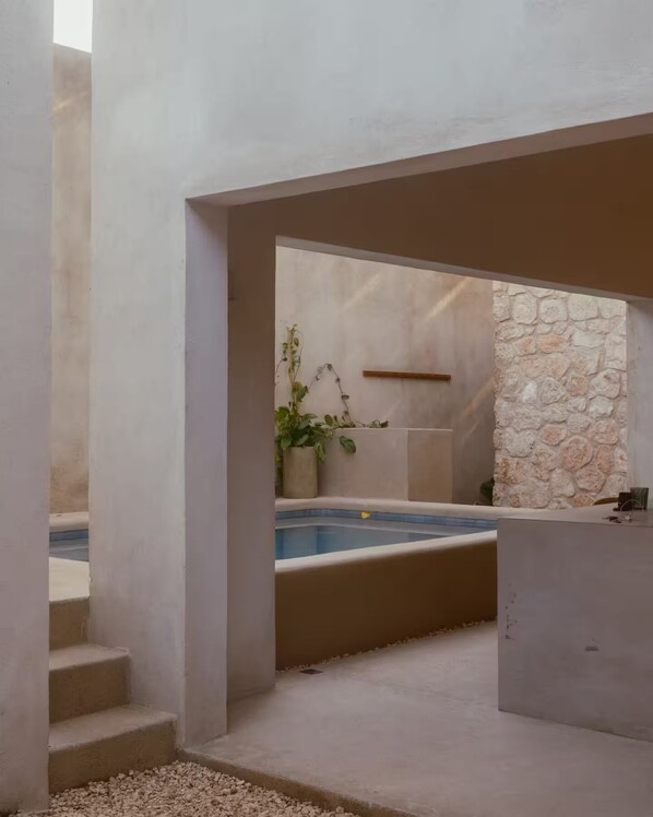 Ein moderner Poolbereich im Freien mit einer Steinwand, einem Blumentopf und einer Betonkonstruktion.