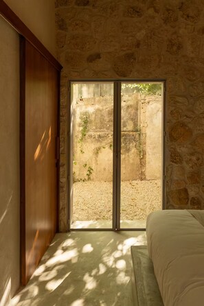 A room with a stone wall, a wooden door, a bed, and a sliding glass door leading to an outdoor area. - Casa Meridiano 48, 2-Bedroom Accommodation (Mérida)