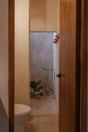 A narrow hallway with a toilet on the left, a wooden door on the right, and a plant in the center. - Casa Meridiano 48, 2-Bedroom Accommodation (Mérida)