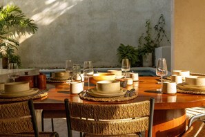 A dining table set with plates, glasses, and a bowl, surrounded by wicker chairs. - Casa Meridiano 48, 2-Bedroom Accommodation (Mérida)