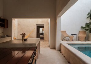 A modern kitchen with a wooden table and chairs, a hammock, and a view of a pool area with lounge chairs. - Casa Meridiano 48, 2-Bedroom Accommodation (Mérida)