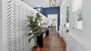 Un pasillo con pared de blanco diseño en espiga, una consola negra, una planta en maceta y suelo de madera.