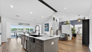 Una cocina moderna con una isla grande, un comedor con vistas y una escalera que lleva a un balcón.