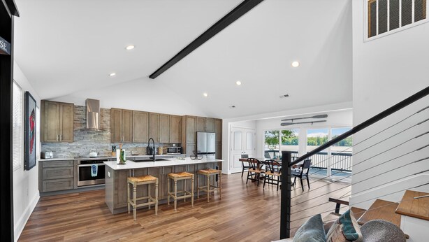 Una cocina moderna con armarios de madera, una isla central con taburetes y una escalera que lleva a un balcón.