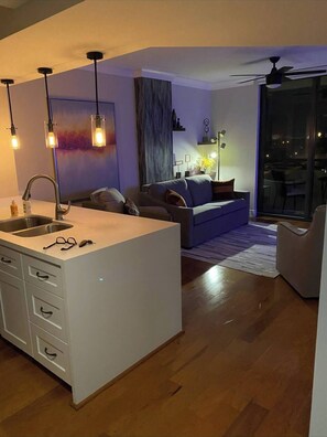 Eine moderne Küche mit einer zentralen Kochinsel, einem Essbereich mit einer Couch und einer großen Glastür zum Balkon.