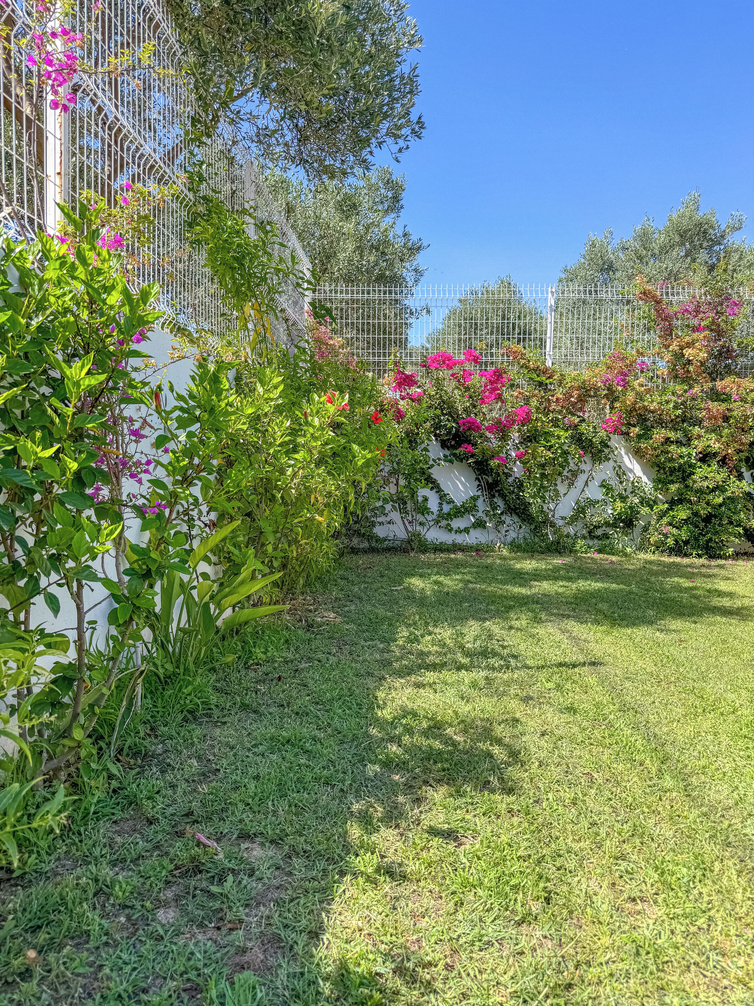 Un jardín bien cuidado con una cerca blanca, césped verde exuberante y plantas con flores.