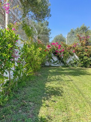 Un jardín bien cuidado con una cerca blanca, césped verde exuberante y plantas con flores.
