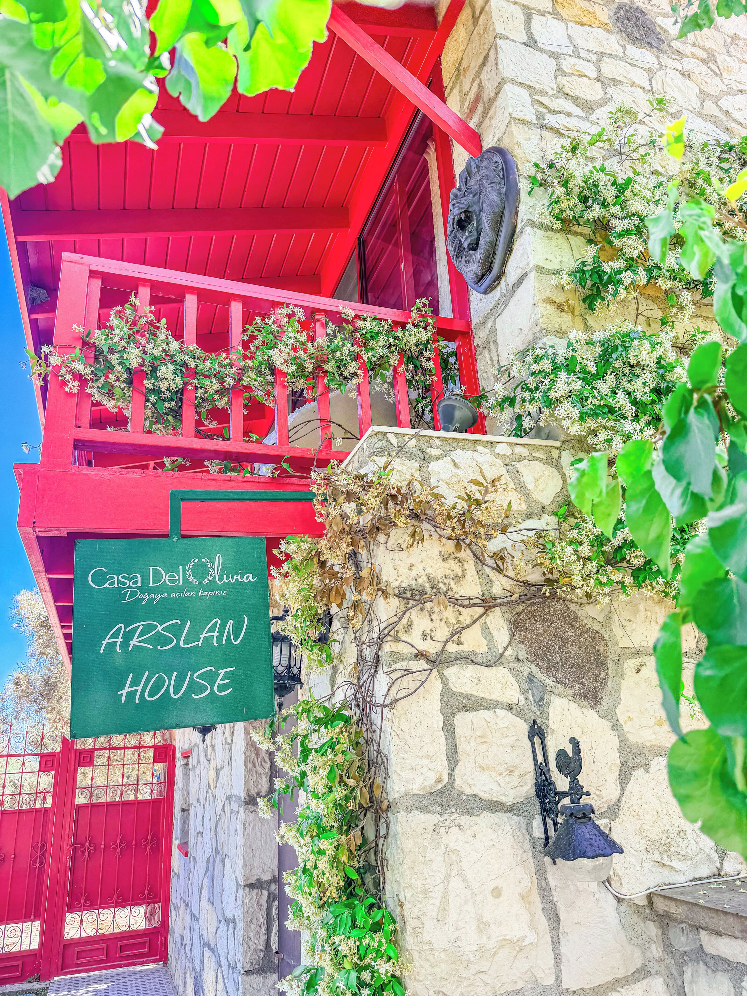 A red building with a sign reading 'Casa Del Olivia Dogaya acilan kapimiz ARSLAN HOUSE'.
