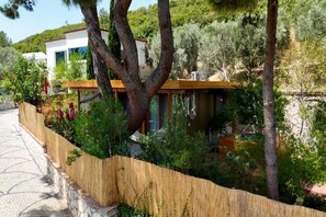 Une maison moderne dotée d’une terrasse en bois, entourée d’arbres et d’un mur de pierres.
