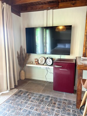 A living room with a flat-screen TV mounted on the wall, a red VESTEL refrigerator, a clock, a vase with dried plants, and a patterned rug. - Casa Del Olivia (Seferihisar)