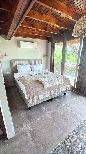 Un dormitorio con una cama grande, techo de madera, una ventana y aire acondicionado de pared.